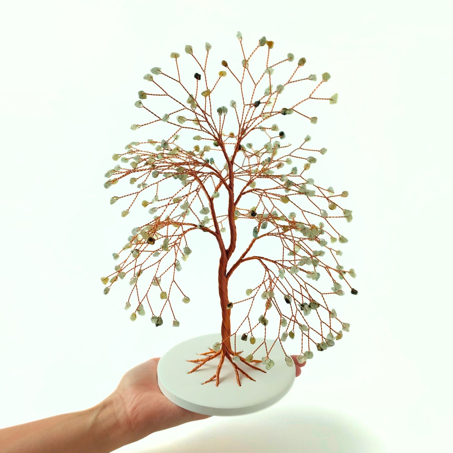 Hand holding a decorative tree with prehnite crystal on a white background