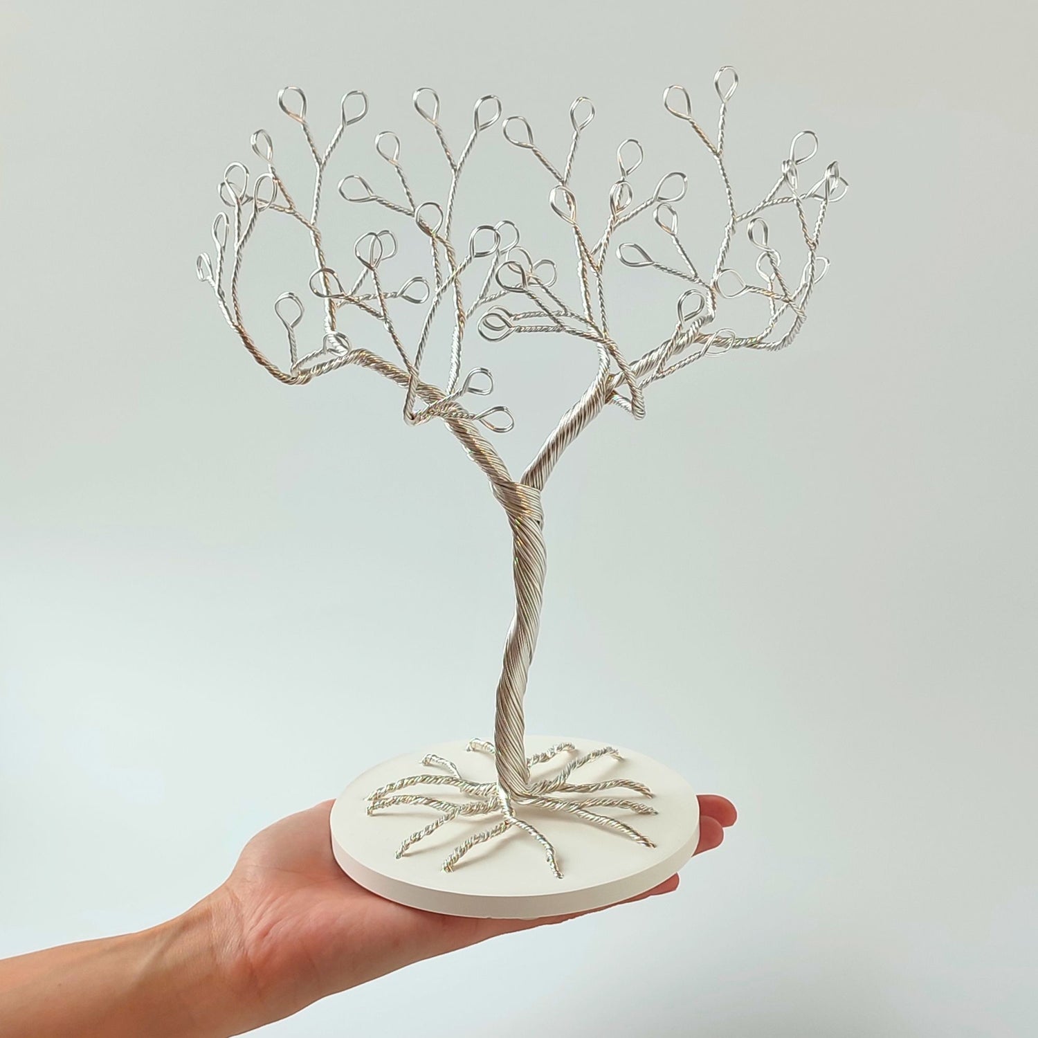 Silver wire tree sculpture on a white base held by a hand against a light gray background