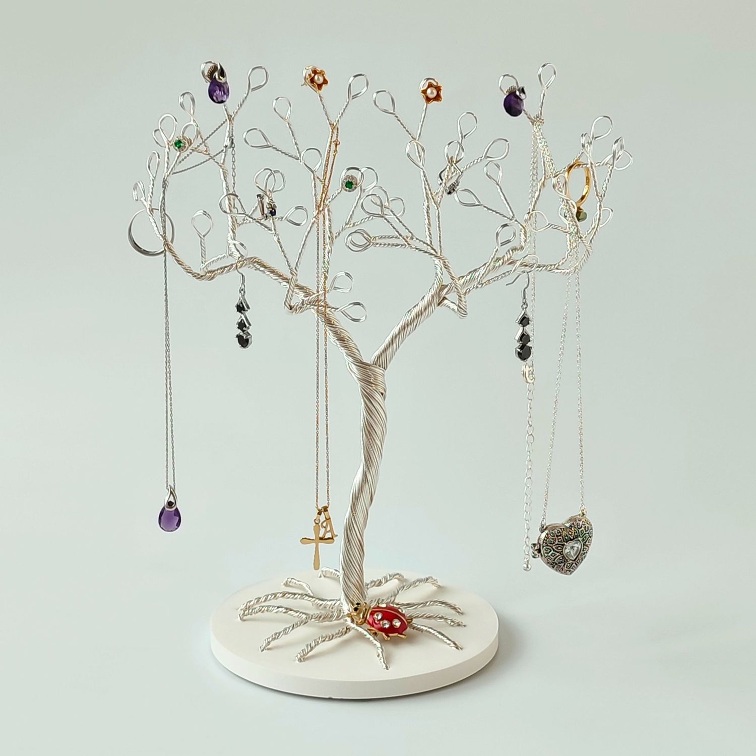 Jewelry tree stand with various necklaces and pendants on a light gray background