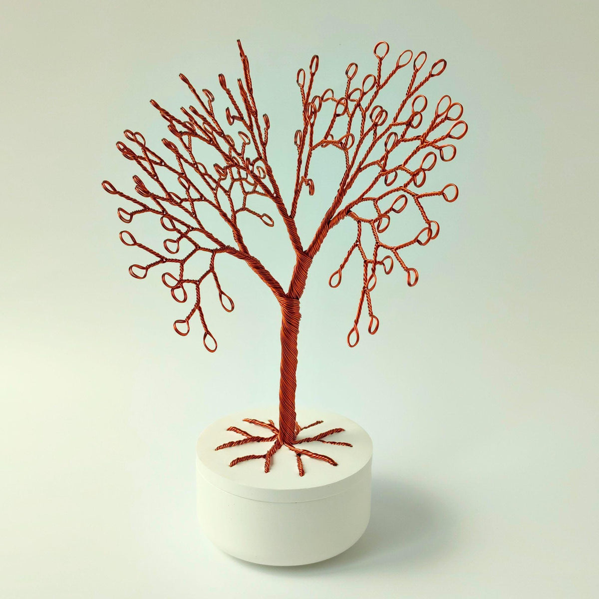 Bare copper wire tree in a white lidded bowl on a light green background