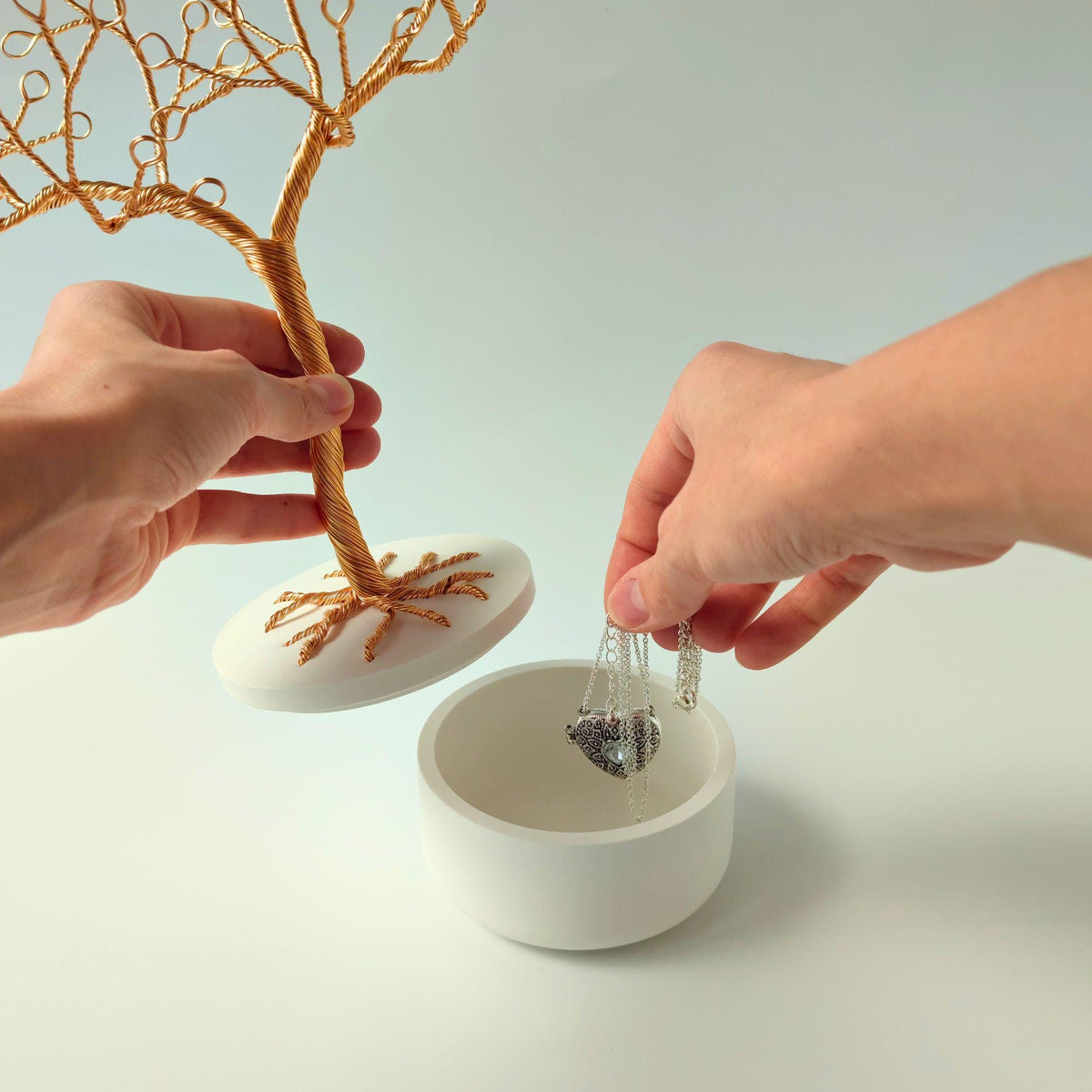 Hand lifting the tree and lid to show a necklace stored in the bowl