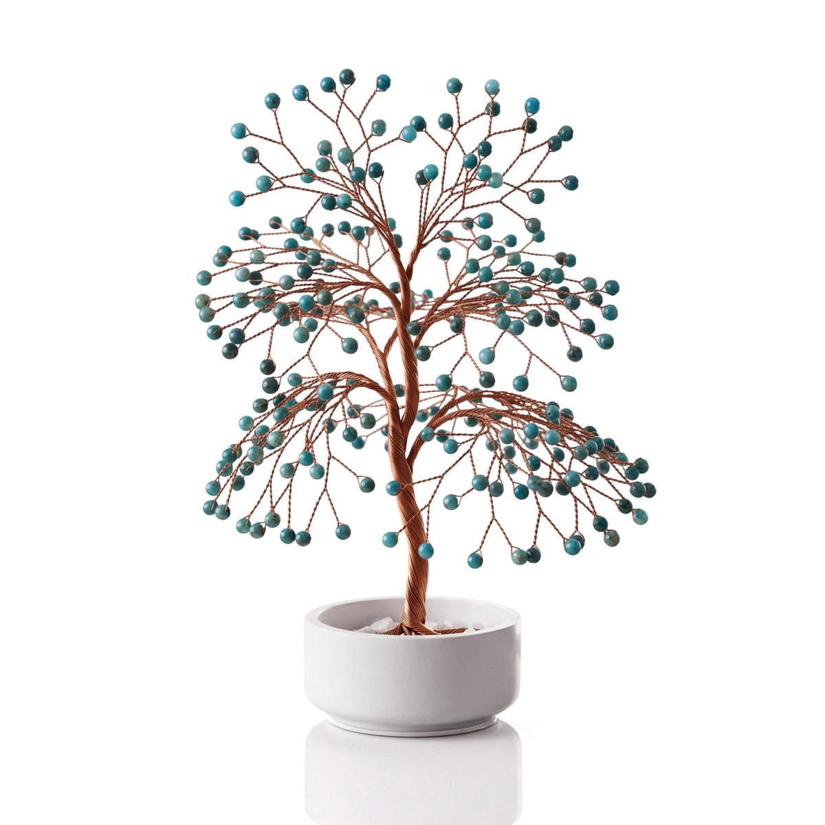 Copper wire tree with polished teal blue apatite spheres in a plain white ceramic bowl