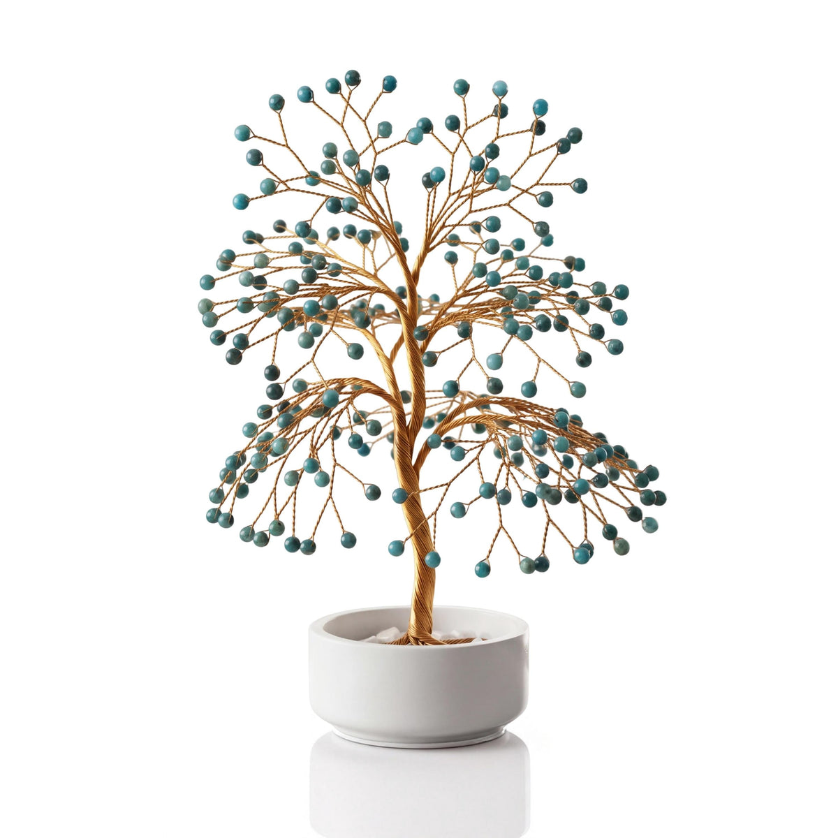 Gold-plated wire tree with polished teal blue apatite spheres in a white ceramic bowl