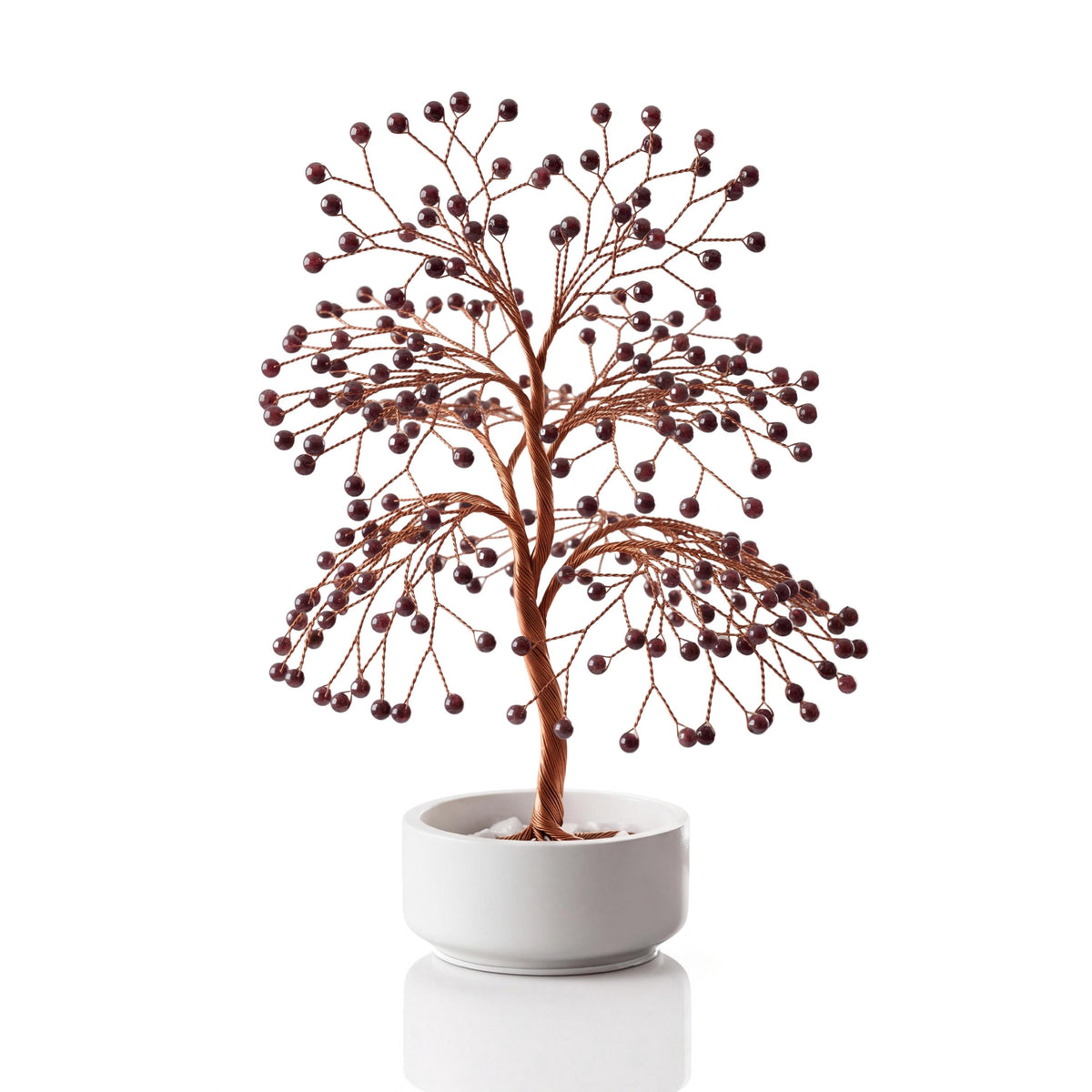 Copper wire tree with polished deep red garnet beads in a plain white ceramic bowl