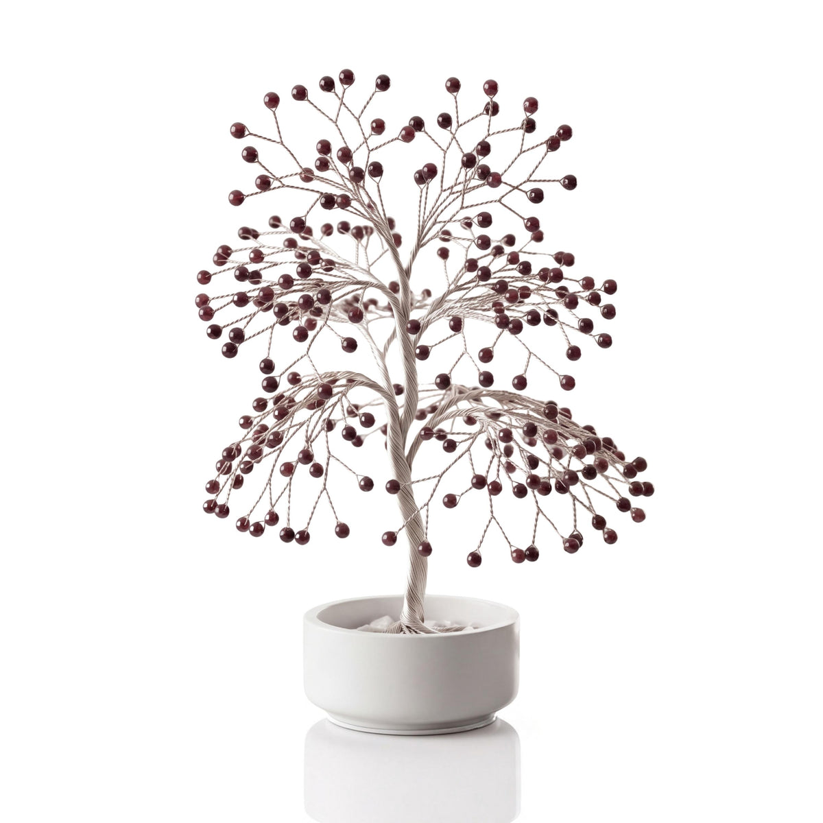 Silver-plated wire tree with polished deep red garnet beads in a white ceramic bowl