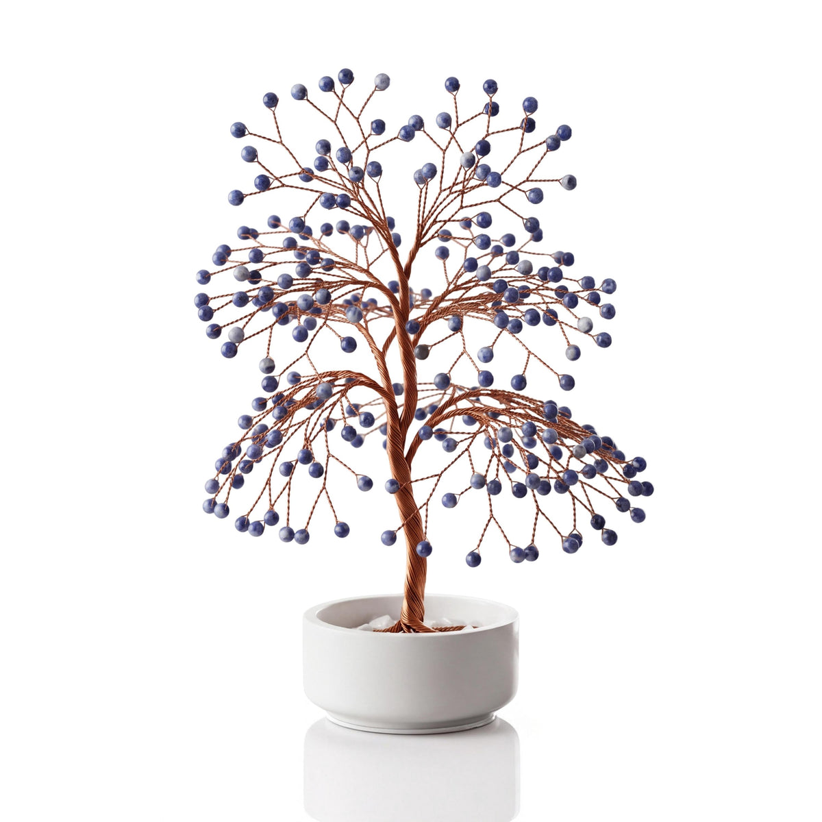 Copper wire tree with polished deep royal blue sodalite spheres in a plain white ceramic bowl