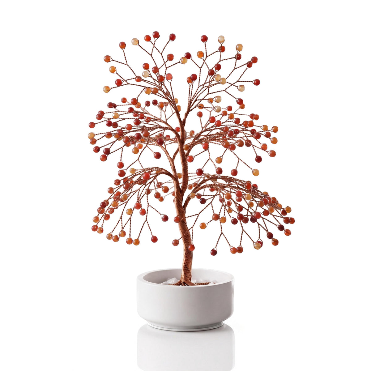 Copper wire tree with polished mixed red and orange carnelian spheres in a plain white ceramic bowl