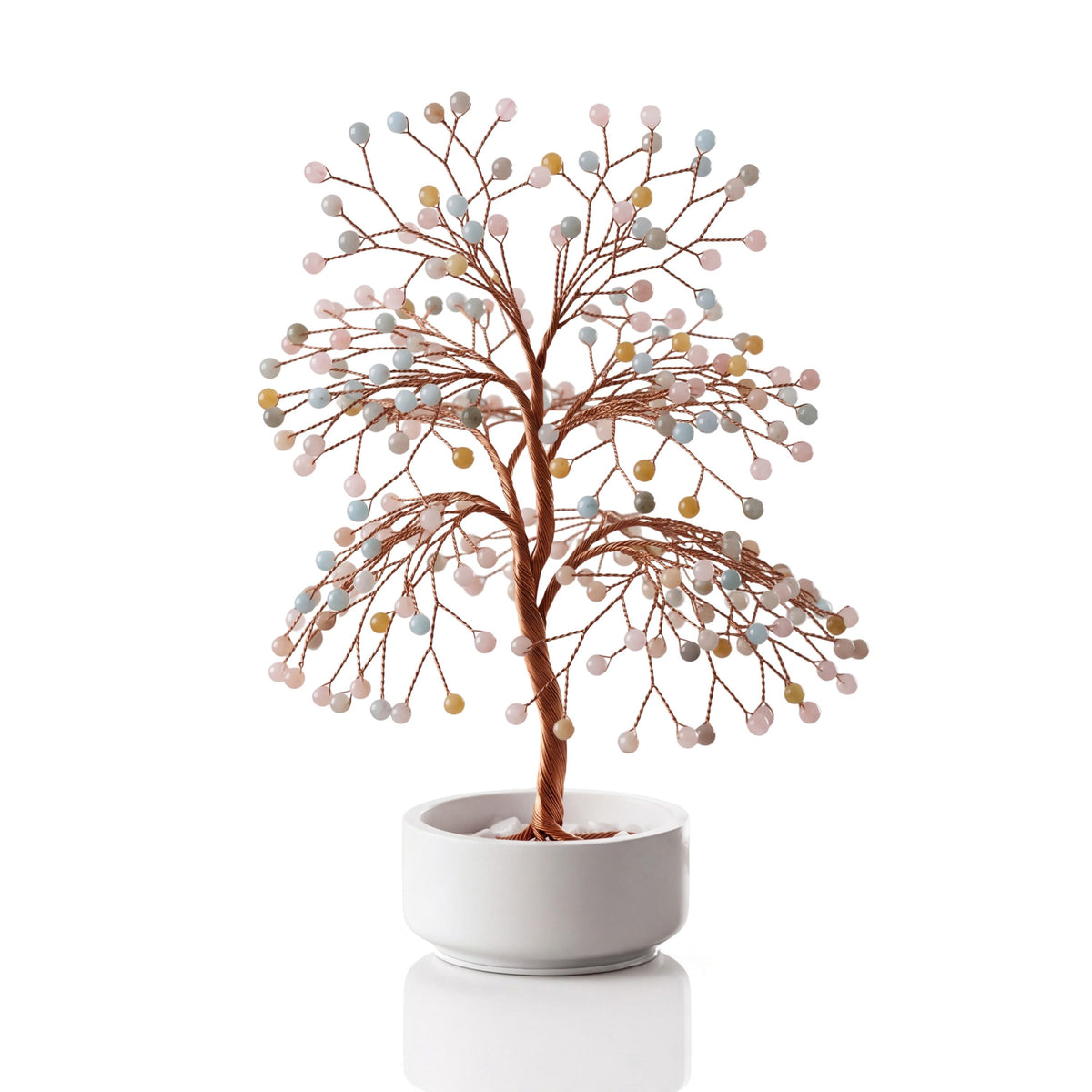 Copper wire tree with polished pastel morganite, heliodor and aquamarine spheres in a plain white ceramic bowl