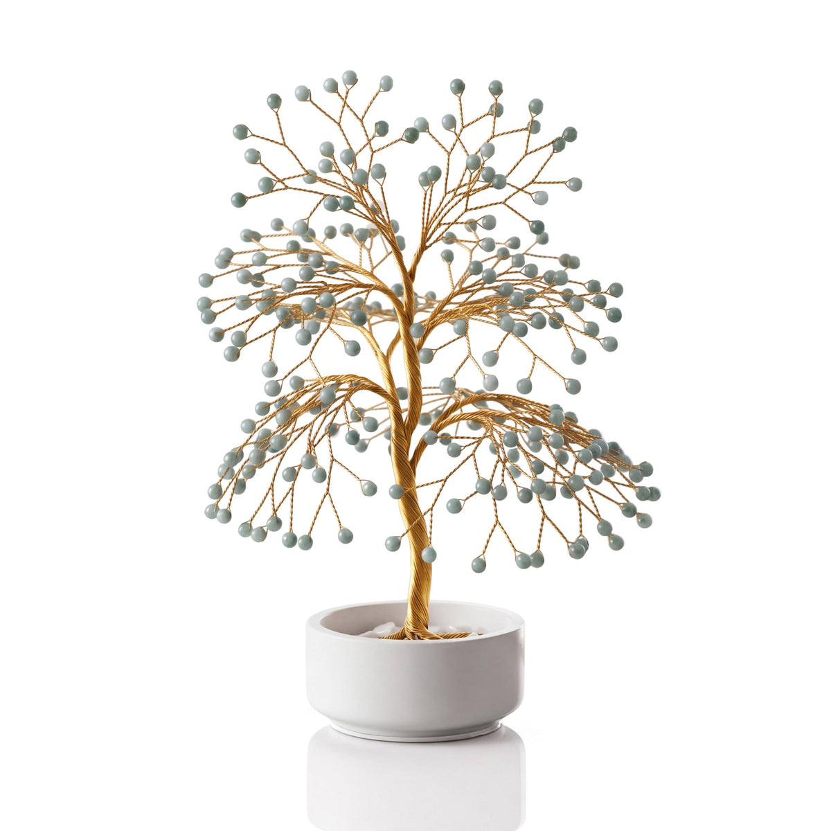 Gold-plated wire tree with polished pale green Burmese jadeite beads in a white ceramic bowl