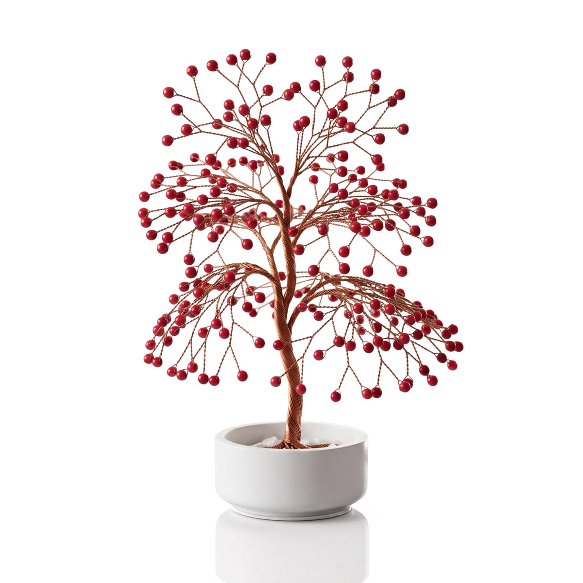 Copper wire tree with polished red coral spheres in a plain white ceramic bowl