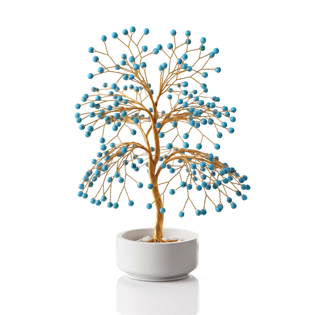 Gold-plated wire tree with polished turquoise blue howlite spheres in a white ceramic bowl