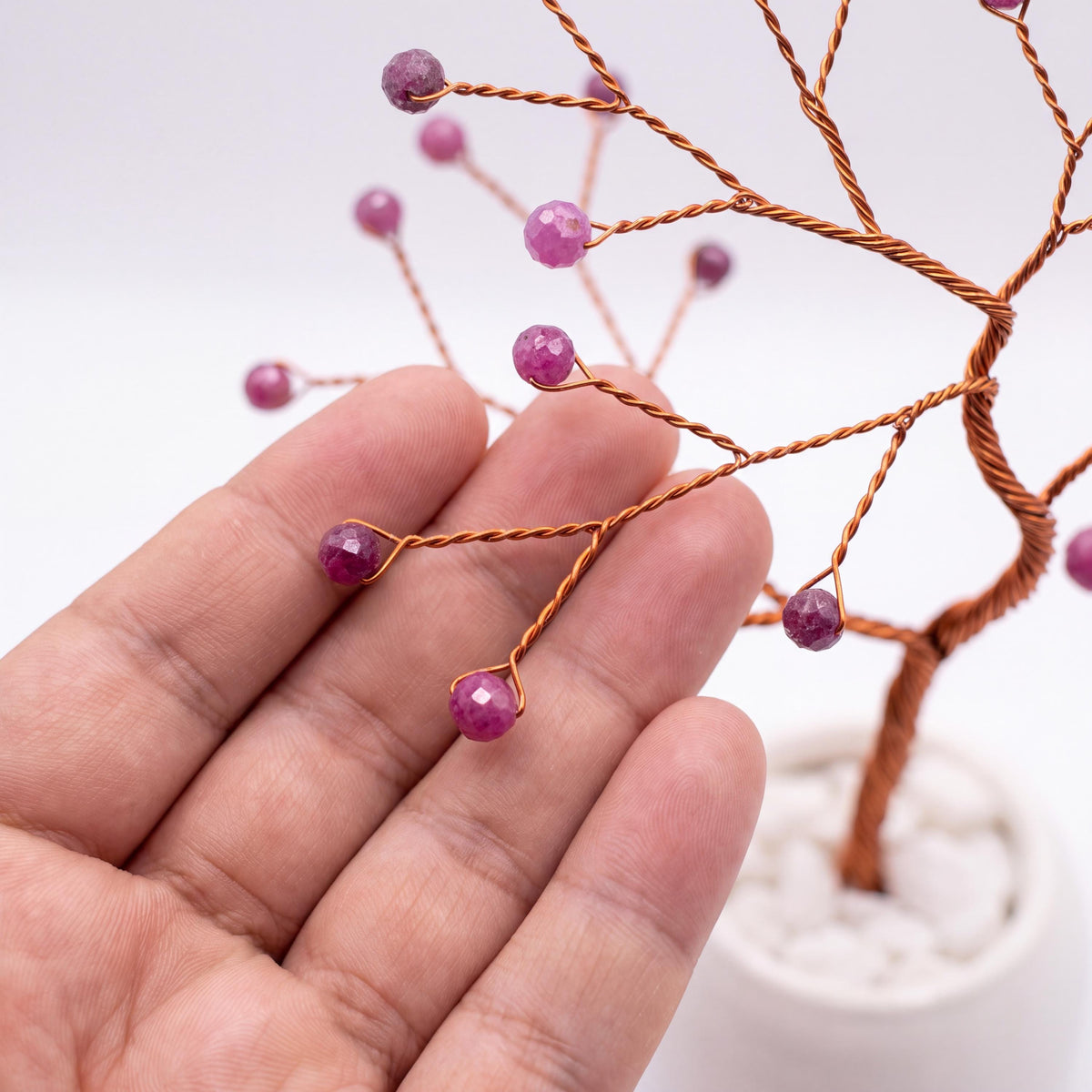 Close-up of a hand holding a branch of the copper wire tree with faceted ruby beads