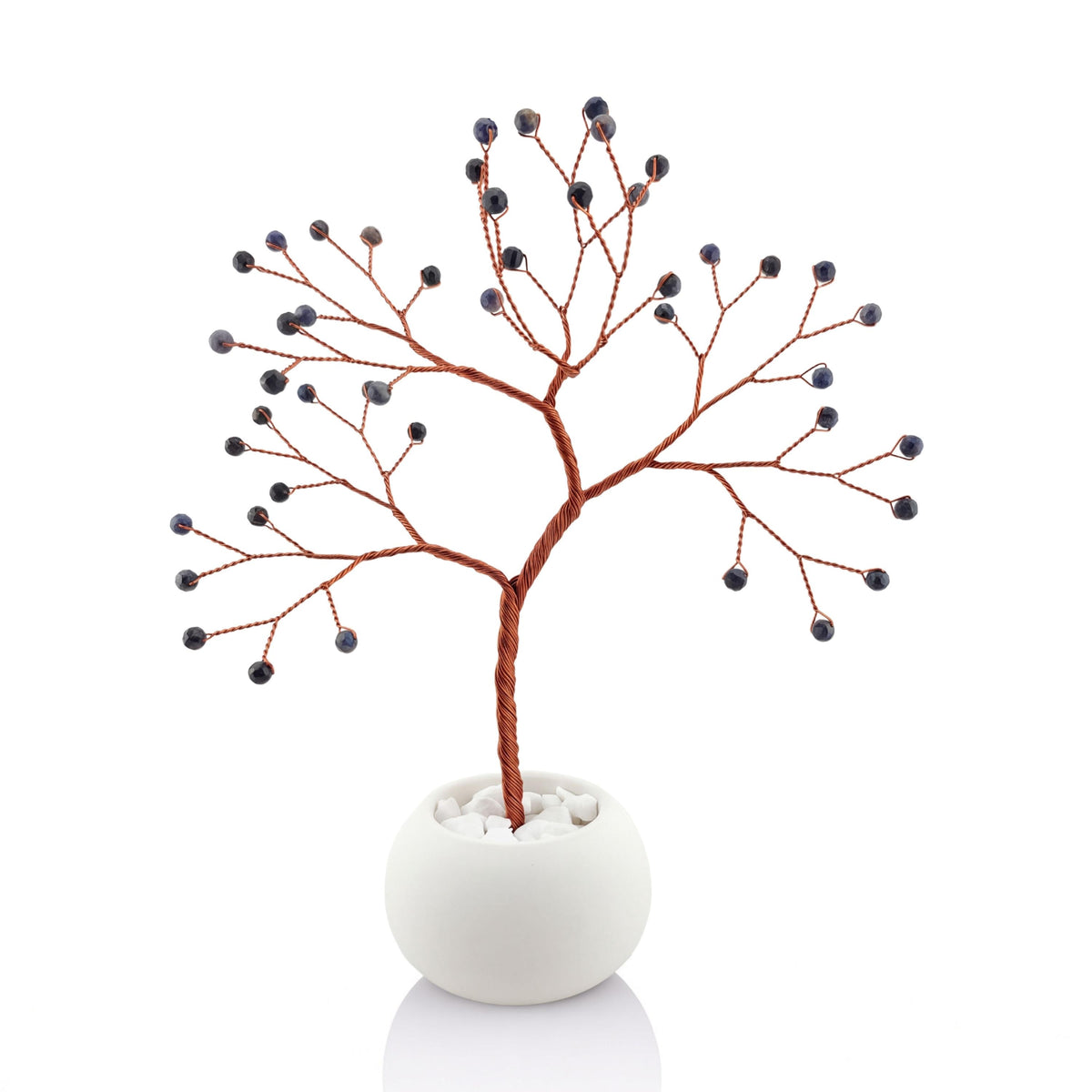 Copper wire tree with dark navy faceted sapphire beads in a plain white bowl filled with white pebbles