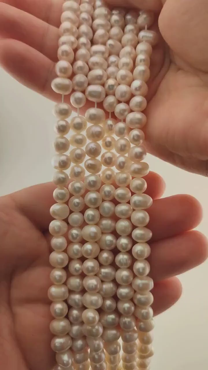 Strands of natural white freshwater pearls held in two hands, the pearls used for the tree
